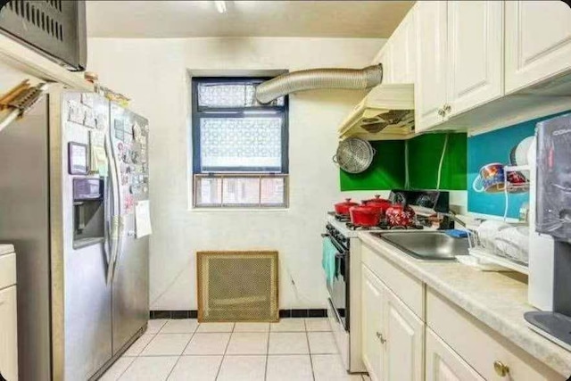 kitchen featuring sink, white cabinetry, stainless steel fridge with ice dispenser, light tile patterned floors, and white range with gas cooktop