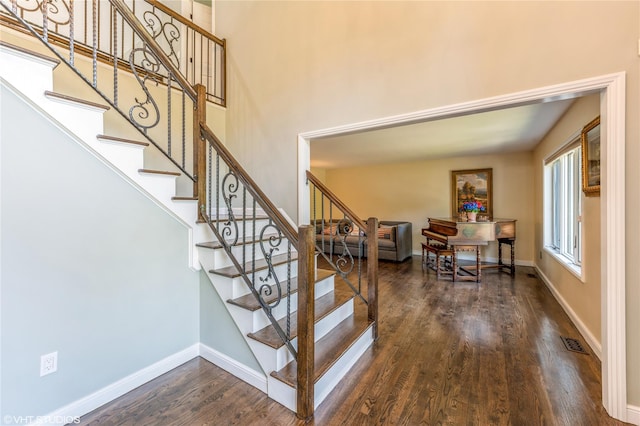 stairway with a towering ceiling, wood finished floors, visible vents, and baseboards