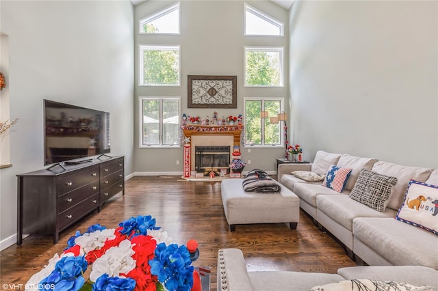 living room featuring dark wood-style flooring, a glass covered fireplace, a towering ceiling, and baseboards