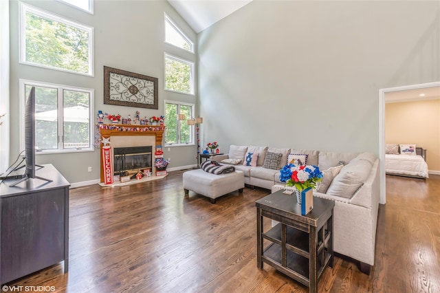 living area with dark wood-type flooring, a glass covered fireplace, plenty of natural light, and high vaulted ceiling