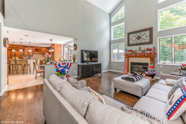 living area with high vaulted ceiling, a glass covered fireplace, dark wood-style flooring, and baseboards