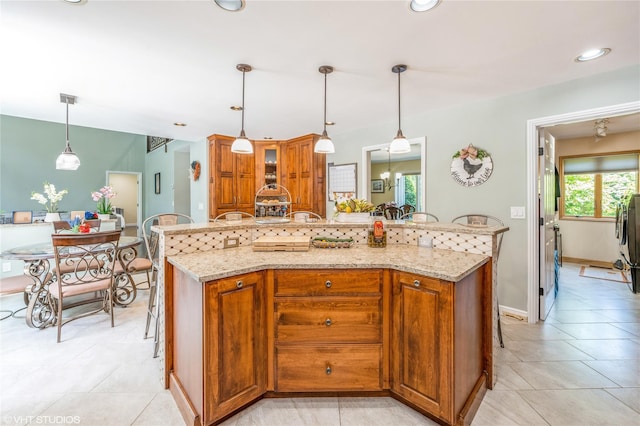 kitchen with brown cabinetry, a breakfast bar, glass insert cabinets, and light stone counters