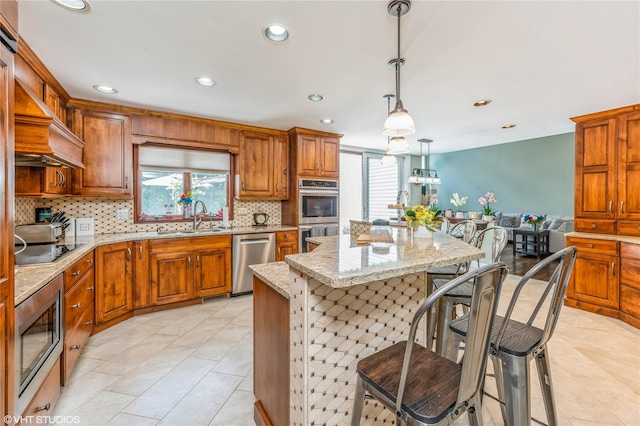 kitchen with a breakfast bar area, a sink, appliances with stainless steel finishes, brown cabinets, and tasteful backsplash