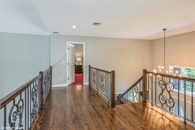 hall with baseboards, visible vents, wood finished floors, an upstairs landing, and a notable chandelier