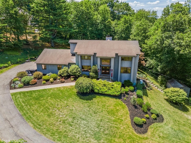 view of front of house featuring aphalt driveway, a chimney, a front lawn, and roof with shingles