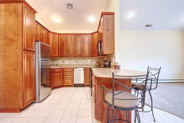 kitchen featuring a breakfast bar, appliances with stainless steel finishes, light tile patterned flooring, vaulted ceiling, and kitchen peninsula