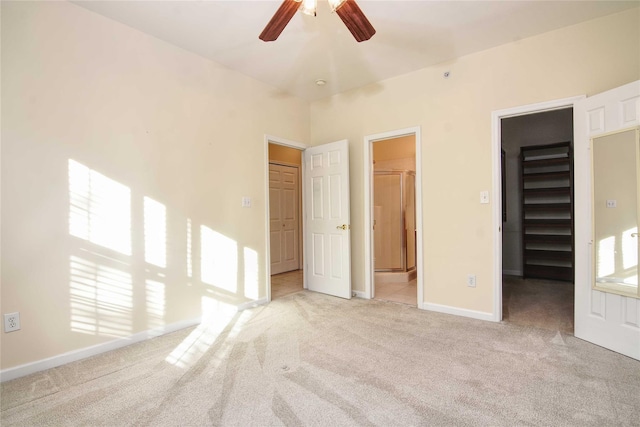 unfurnished bedroom featuring light carpet, a walk in closet, a closet, and ceiling fan