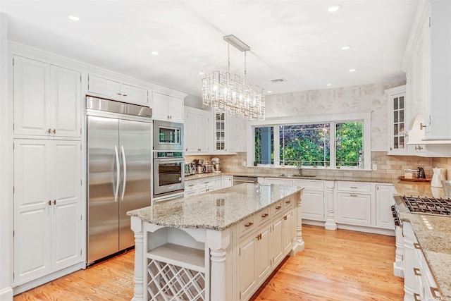 kitchen with a kitchen island, white cabinets, hanging light fixtures, built in appliances, and light wood-type flooring