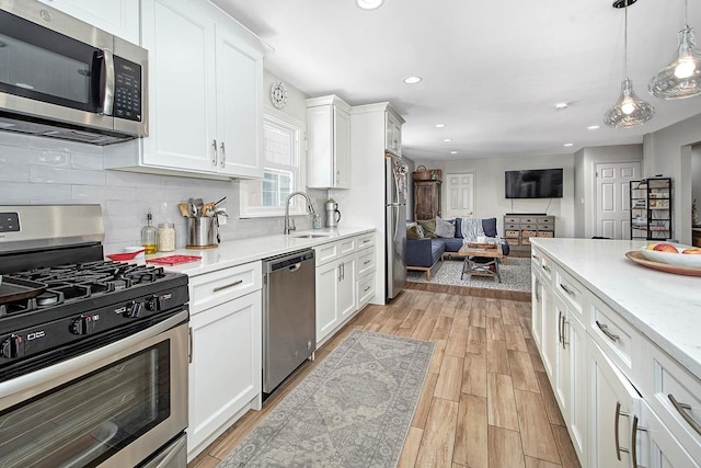 kitchen featuring decorative light fixtures, sink, white cabinets, stainless steel appliances, and light wood-type flooring