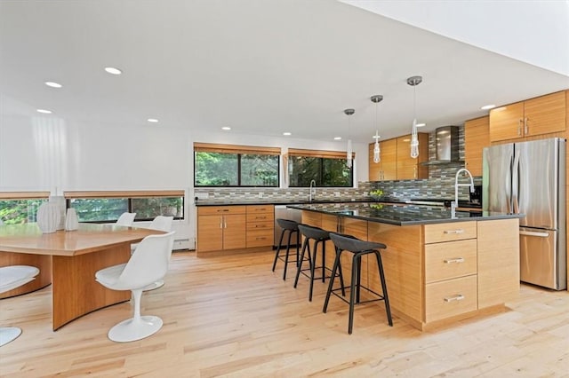 kitchen with wall chimney exhaust hood, a breakfast bar area, a center island, hanging light fixtures, and appliances with stainless steel finishes