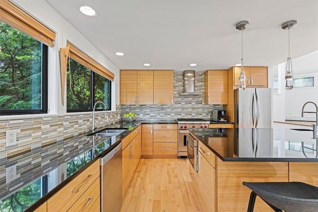 kitchen featuring sink, a breakfast bar area, decorative light fixtures, stainless steel appliances, and wall chimney range hood