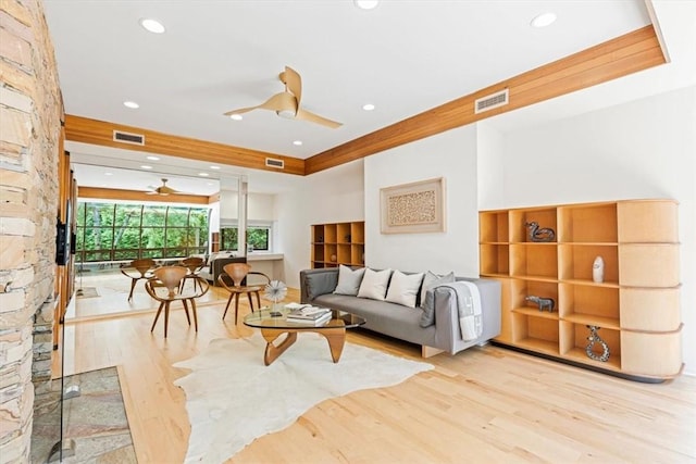 living room with light hardwood / wood-style floors, a raised ceiling, and ceiling fan