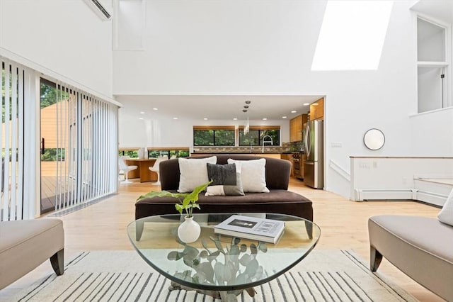 living room featuring sink, a skylight, a high ceiling, and light wood-type flooring