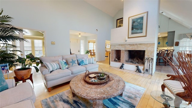 living room featuring a tiled fireplace, high vaulted ceiling, a wealth of natural light, and light wood-type flooring