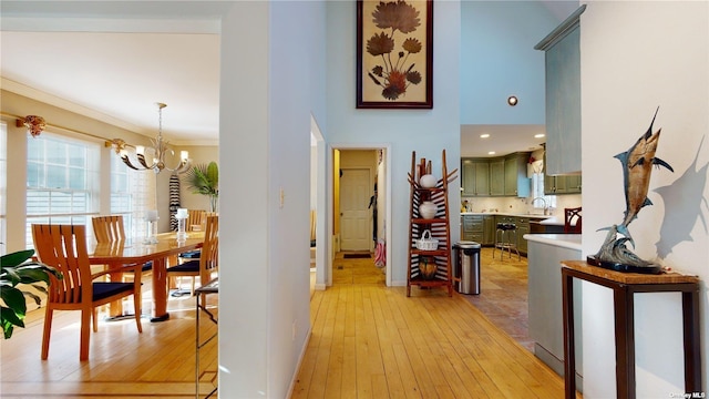 corridor with sink, an inviting chandelier, ornamental molding, light hardwood / wood-style floors, and a high ceiling