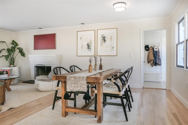 dining area featuring a fireplace, light hardwood / wood-style flooring, and ornamental molding