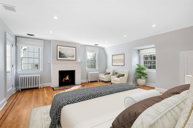 bedroom featuring light wood-type flooring, radiator, and a fireplace