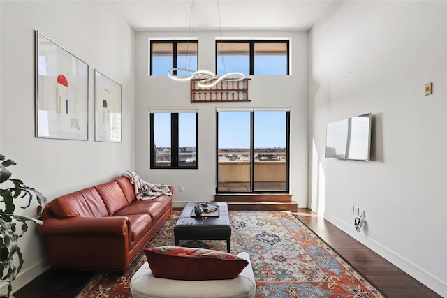 living room featuring a towering ceiling, dark wood-type flooring, and a healthy amount of sunlight