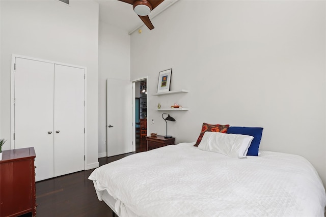 bedroom with ceiling fan, a towering ceiling, dark hardwood / wood-style flooring, and a closet