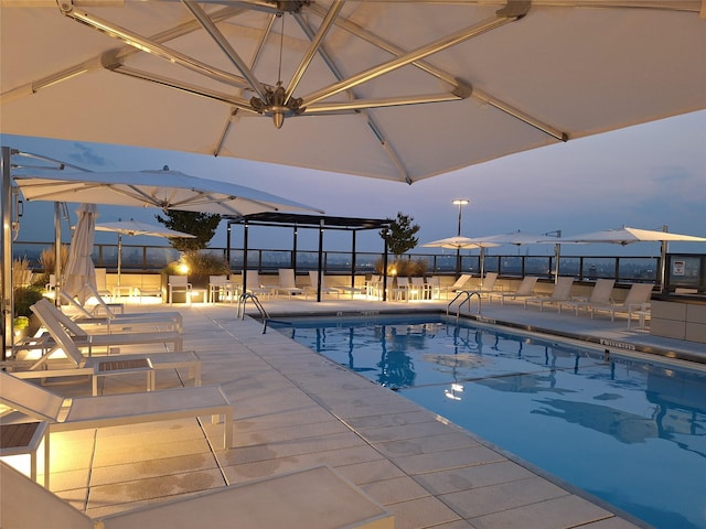 pool at dusk with a patio area and an outdoor kitchen