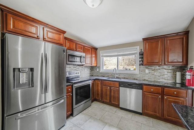 kitchen with sink, light tile patterned floors, dark stone counters, stainless steel appliances, and backsplash