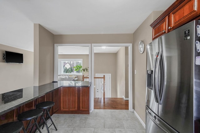 kitchen with dark stone counters, kitchen peninsula, stainless steel fridge with ice dispenser, and light tile patterned floors