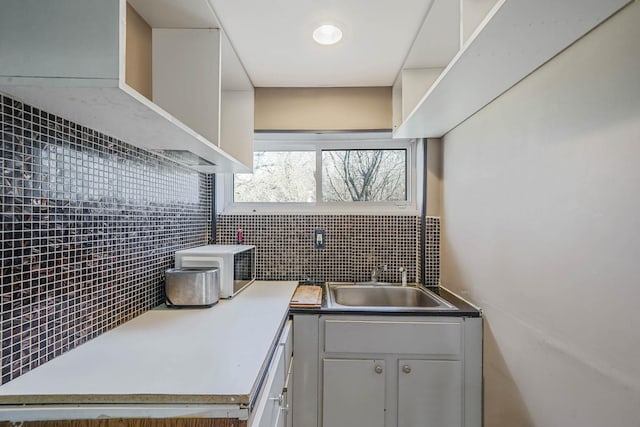 kitchen with tasteful backsplash, white cabinetry, sink, and wall chimney range hood