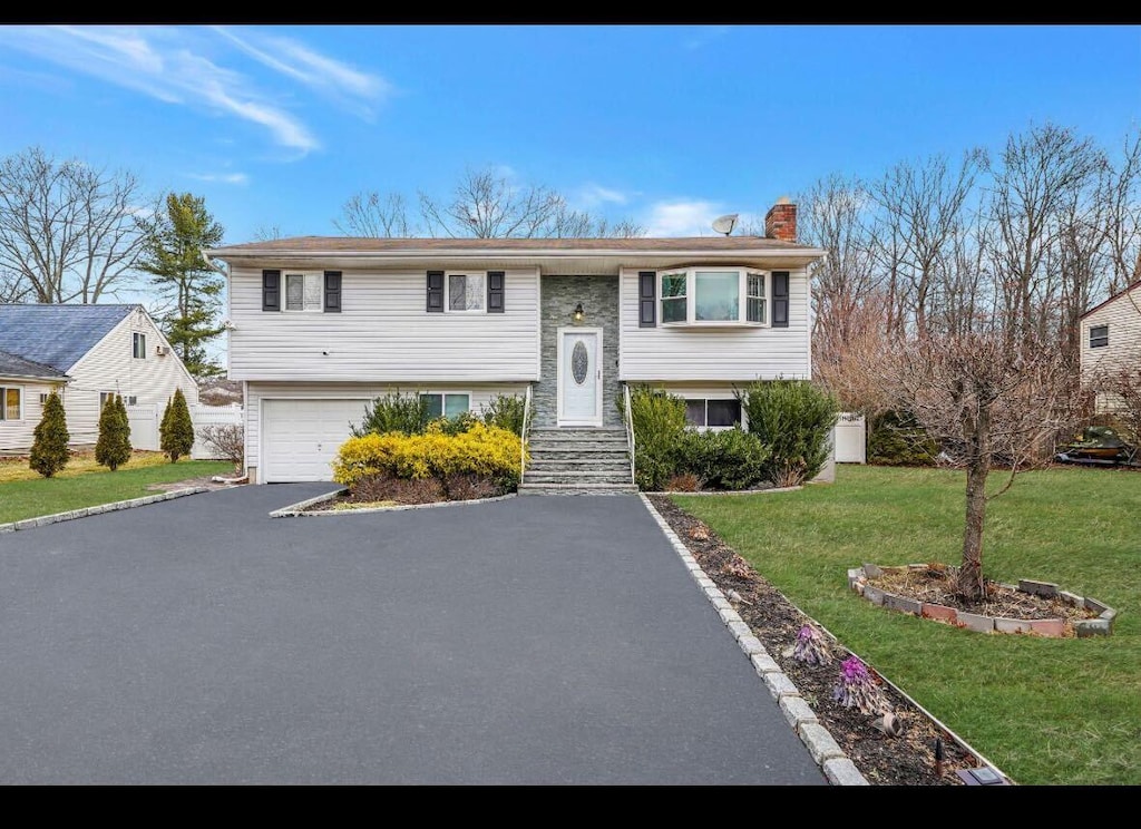 raised ranch featuring a garage and a front lawn