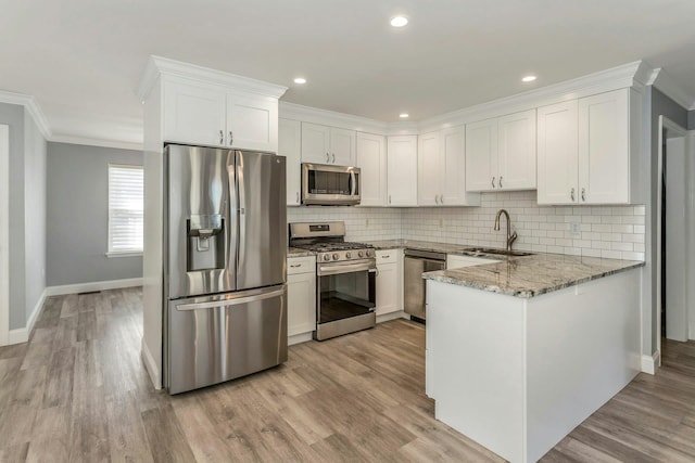 kitchen featuring sink, white cabinetry, stainless steel appliances, light stone counters, and kitchen peninsula