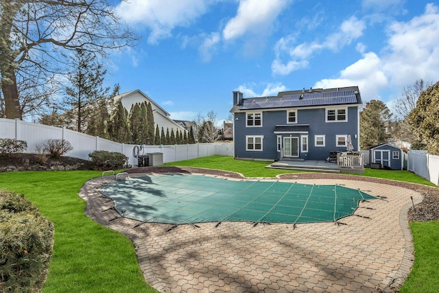 back of property featuring a pool side deck, a storage shed, a yard, and solar panels