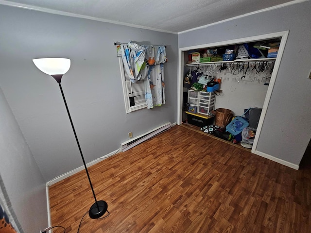 unfurnished bedroom with a baseboard heating unit, wood finished floors, baseboards, ornamental molding, and a closet