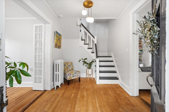 foyer featuring radiator, hardwood / wood-style floors, ornamental molding, baseboards, and stairs