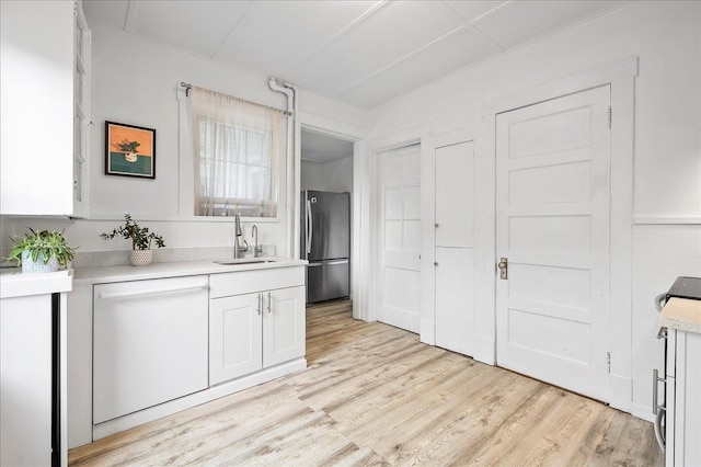 kitchen featuring white dishwasher, a sink, white cabinetry, light countertops, and freestanding refrigerator