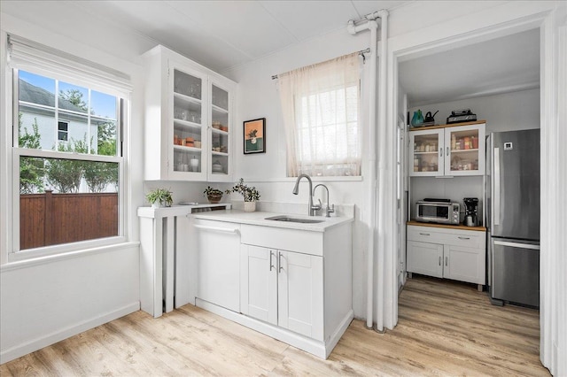 bar with appliances with stainless steel finishes, a sink, and light wood-style floors