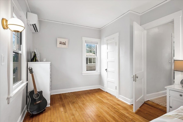 bedroom with light wood-type flooring, ornamental molding, a wall mounted air conditioner, and baseboards