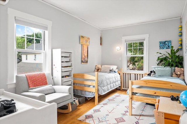 bedroom featuring light wood-type flooring, radiator heating unit, multiple windows, and ornamental molding