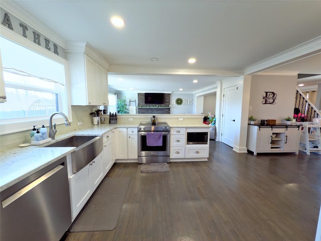 kitchen with appliances with stainless steel finishes, sink, white cabinets, light stone counters, and kitchen peninsula