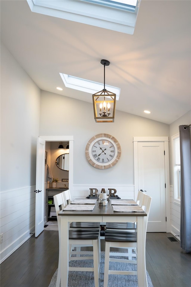 dining space with a notable chandelier, dark wood-type flooring, and lofted ceiling with skylight