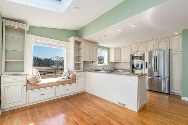 kitchen featuring a skylight, stainless steel appliances, kitchen peninsula, and backsplash