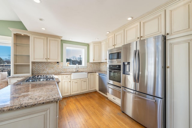 kitchen featuring light stone counters, cream cabinets, stainless steel appliances, and sink