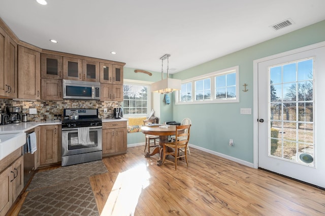 kitchen with pendant lighting, light hardwood / wood-style flooring, appliances with stainless steel finishes, backsplash, and a chandelier