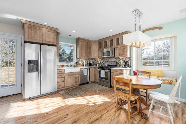 9875 Main Bayview Rd, Southold, NY 11971 - kitchen featuring stainless steel appliances, light wood-style flooring, backsplash, light countertops, and a chandelier
