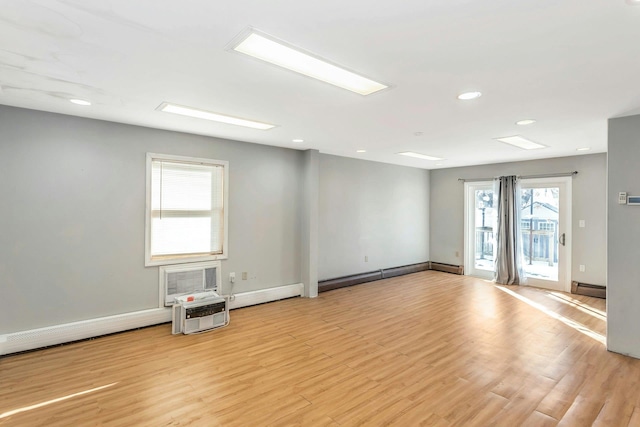 empty room featuring a wall mounted AC, baseboard heating, and light hardwood / wood-style floors