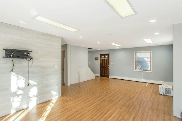 interior space with a baseboard heating unit, a wall mounted air conditioner, and light hardwood / wood-style flooring