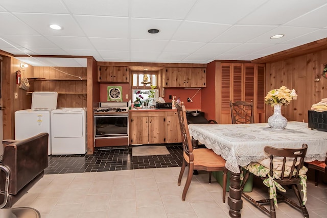 dining area with a paneled ceiling, washer and clothes dryer, and wood walls