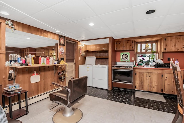 kitchen with wood walls, a baseboard heating unit, independent washer and dryer, a drop ceiling, and gas range oven