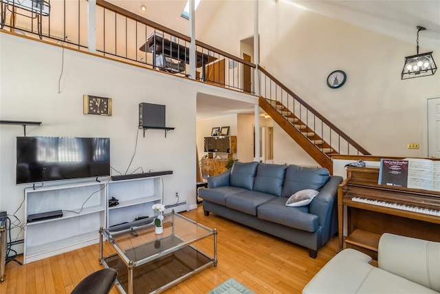 living room with a baseboard heating unit, wood-type flooring, a towering ceiling, and a chandelier