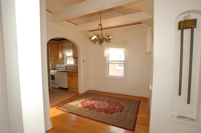 doorway with beamed ceiling, light wood-type flooring, and an inviting chandelier