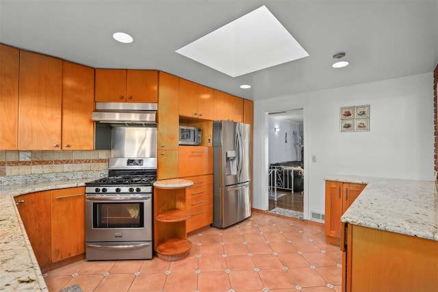 kitchen featuring light tile patterned floors, a skylight, under cabinet range hood, appliances with stainless steel finishes, and backsplash