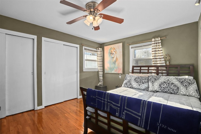 bedroom with two closets, wood-type flooring, and ceiling fan